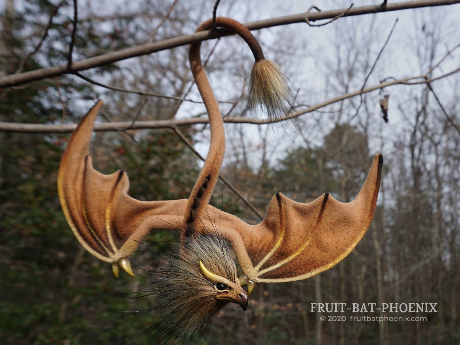 Gold Ochre Eagle Wyrm, a posable dragon art doll, hanging by its tail on a branch